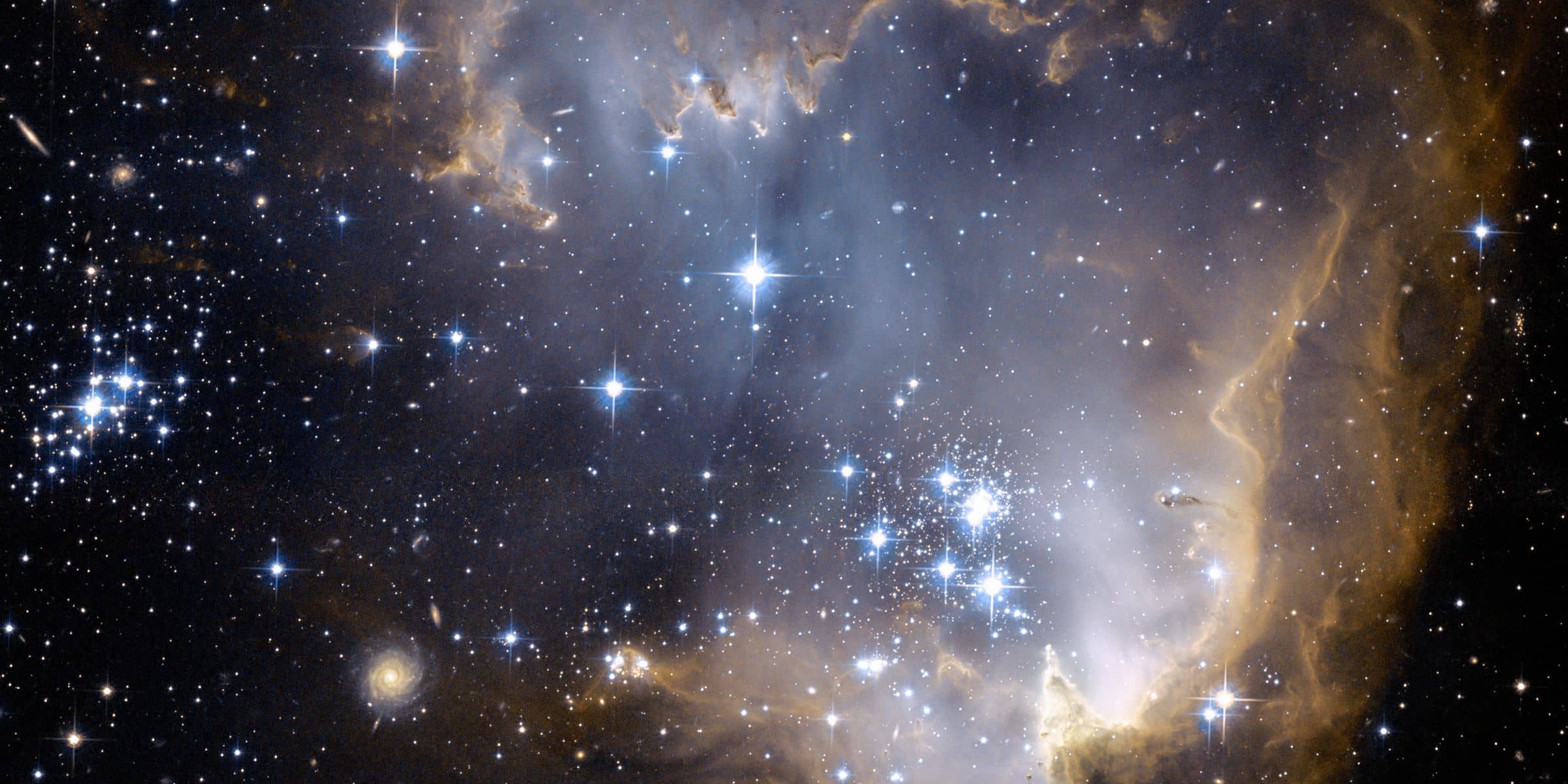 The cluster of blue stars, called NGC 602, formed when a large part of the gas cloud collapsed under gravity and became very dense. The fierce radiation now being produced by these hot, young stars is sculpting the inner rim of the gaseous nebula.